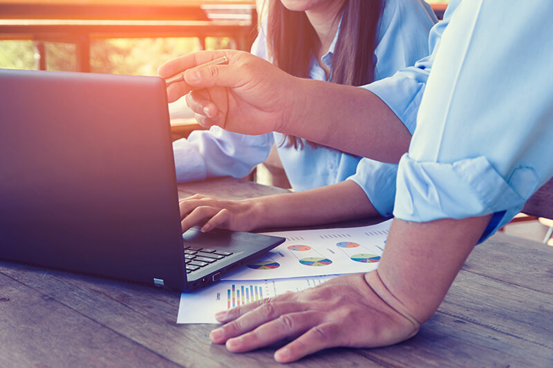 man and woman referencing reports and laptop on wooden table